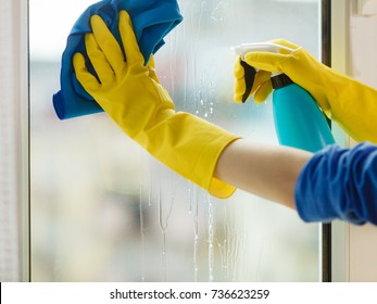 Female hand in yellow gloves cleaning window with blue rag and spray detergent. Spring cleanup, housework concept