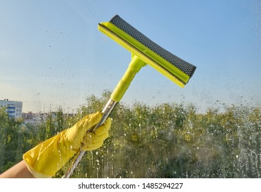 Female Hand In Yellow Gloves Washes A Window With A Window Scraper