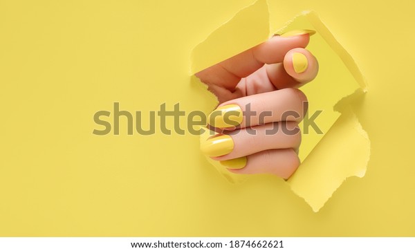Female hand with\
yellow nail design. Glitter yellow nail polish manicure. Woman hand\
on yellow paper\
background.