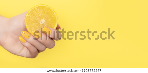 Female hand with yellow nail design. Yellow nail\
polish manicure. Woman hand with yellow lemon on yellow background.\
Copy space