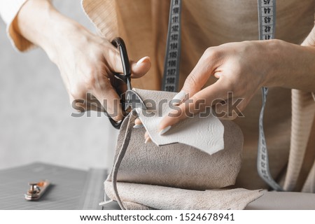 Female handbag designer measuring leather and cutting out details in a workshop studio