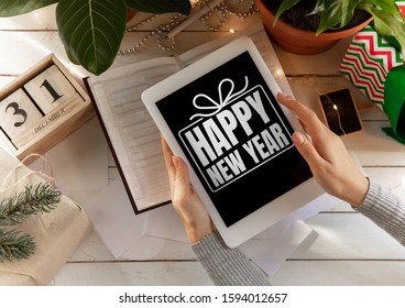 Female hands against wooden table with gift holding tablet with wishes of happy New Year and Merry Christmas. Concept of Christmas, 2020 New Year's, winter mood, holidays. Copyspace, flyer, postcard.