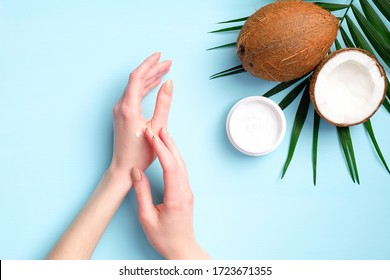 Female hands applying organic cosmetics cream with coconut oil, top view. Skincare, body and hair treatment concept.