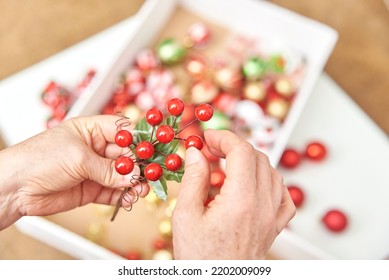 Female Hands With Artificial Sprig Of Holly Berries, Unrecognizable Woman Preparing Christmas Ornaments For Decoration. Bright Composition With Copy Space.