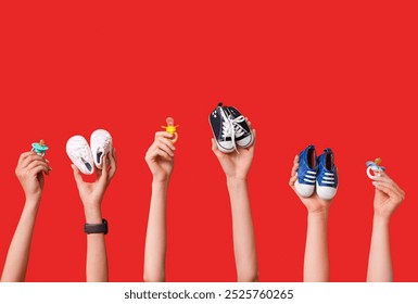 Female hands with baby booties and pacifiers on red background - Powered by Shutterstock