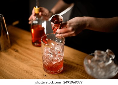 Female hands of a bartender pouring a jigger of brown liquid into a cocktail glass with ice - Powered by Shutterstock