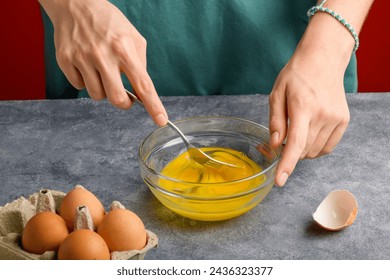 Female hands beat eggs with fork in a glass bowl on a gray kitchen table. Cooking scrambled fresh eggs for breakfast, the process of omelette cooking, close up - Powered by Shutterstock