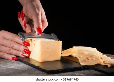 Female hands with beautiful bright manicure cut cheese whetstone by means of a  slicer on  black slate plate