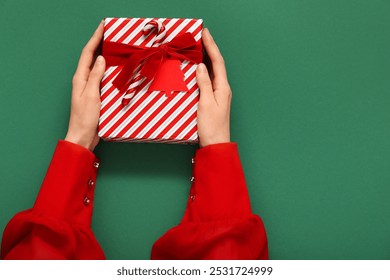 Female hands with beautiful Christmas gift on green background, closeup