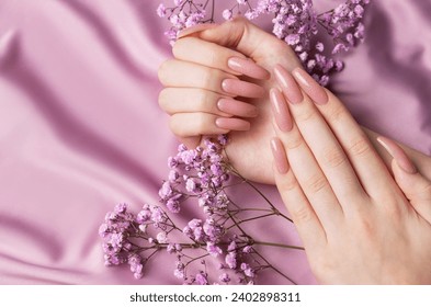 Female hands with beautiful manicure  with gypsofila flowers on pink silk