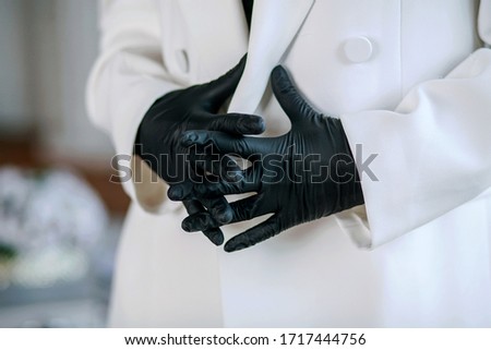 Female hands in black medical gloves are clenched into fists against the background of a white medical suit. Virus protection. Selective Focus Image