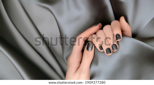 Female hands with\
black nail design. Glitter black nail polish manicure. Woman hands\
on gray fabric\
background
