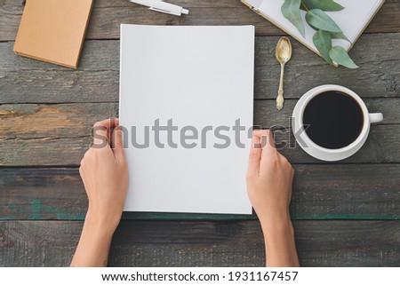 Female hands with blank magazine and cup of coffee on wooden background