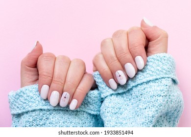 Female hands in blue knitted sweater with beautiful manicure - white ivory nails with flower on pink paper background