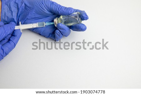 Female hands in blue medical gloves hold a syringe and a bottle of medicine or vaccine