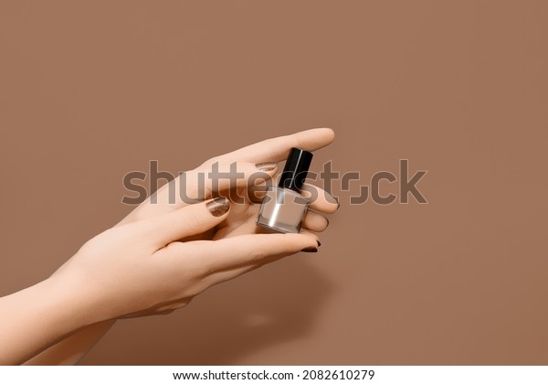 Female hands with brown nail design. Glitter brown\
nail polish manicure. Female hands hold brown nail polish on brown\
background. Copy space.
