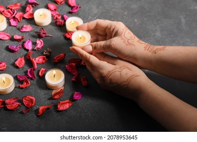 Female hands with burning candles and flower petals for celebration of Divaly on dark background