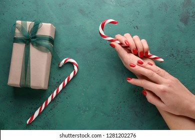 Female hands with candy canes and gift box on green background