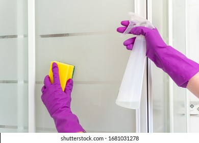 Female hands cleaning white, transparent shower cabin with yellow and green sponge and white spray bottle in bright, pink rubber gloves closeup. - Shutterstock ID 1681031278