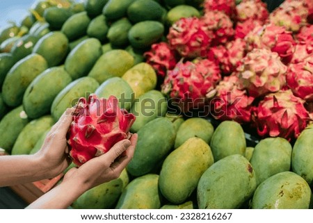 Female hands close-up, holding a dragon fruit against the background of a fruit stand, in a supermarket.