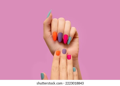 Female hands with colorful nail design. Glitter nail polish manicure: purple, green, pink, and orange. Female model hands with perfect colorful manicure on pink background. Copy space. Place for text.