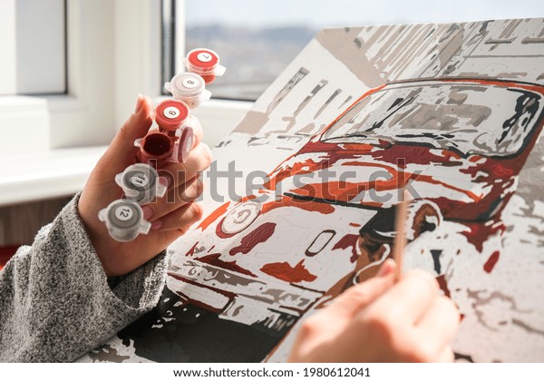 Female hands coloring canvas Picture by numbers\
car and girl. Creative hobby. Painting for beginners. Leisure\
activity for stay home isolation, anti-stress idea. Meditation,\
relax concept