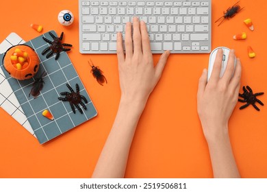 Female hands with computer keyboard, mouse, notebooks and candies for Halloween on color background, closeup