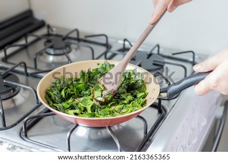 Female hands cooking ora-pro-nobis in frying pan. Stirring wooden spoon. Pereskia aculeata is a popular vegetable in parts of Brazil Imagine de stoc © 