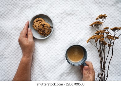 Female Hands With A Cup Of Coffee And A Plate Of Chocolate Biscuits On A Bed Cover. Top View.