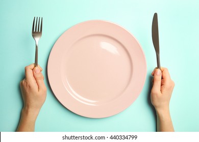 Female hands with cutlery and empty plate on turquoise background