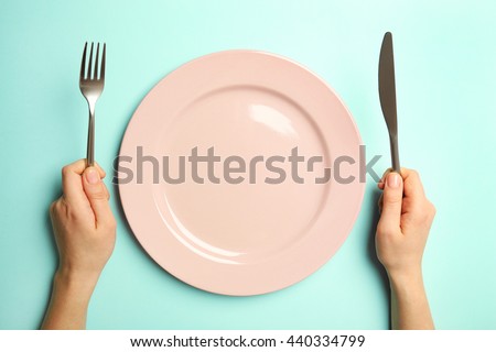 Female hands with cutlery and empty plate on turquoise background
