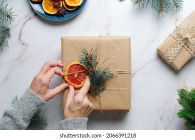 Female hands decorates Christmas present using dried oranges. Overhead view. Eco friendly DIY Christmas decoration for Christmas gifts.
