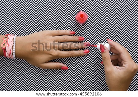 Female hands doing nail polish in coral color with summer bracelets