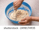 Female hands and dough in a blue metal bowl. Female chef preparing dough on kitchen table, closeup. Woman stirs around spoon in bowl flour. Woman kneading dough by hand yeast dough.