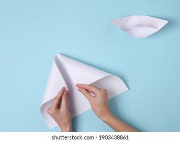 Female Hands Fold Origami Boat On A Blue Background. Top View