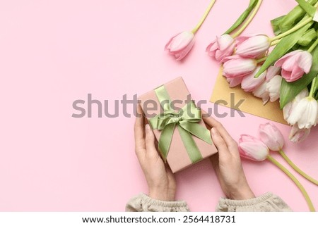 Female hands with gift box, bouquet of beautiful tulips and envelope on pink background. International Women's Day