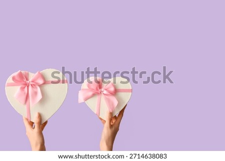 Female hands with gift boxes in shape of heart on lilac background. Valentine's Day celebration