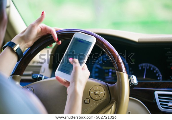 Female hands with gold black\
watch holding leather steering wheel and white smartphone in\
car