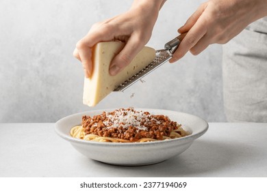 Female hands grating cheese into bowl of pasta. Appetizing pasta with Bolognese sauce in bowl. - Powered by Shutterstock