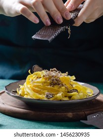 Female hands grating parmesan cheese, black truffle onto pasta tagliatelle.
