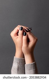 Female hands in gray knitted sweater with beautiful manicure - dark black nails on gray background. Nail care concept
