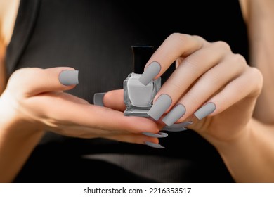 Female hands with gray nail design. Mate gray nail polish manicure. Female model in black dress with perfect gray manicure hold gray nail polish bottle.
