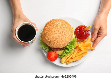 Female hands with hamburger and French fries on white background
