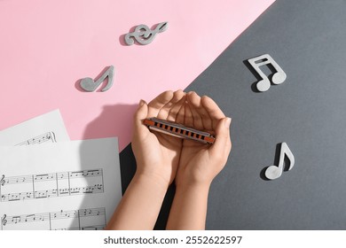 Female hands with harmonica, music sheets and note signs on color background - Powered by Shutterstock