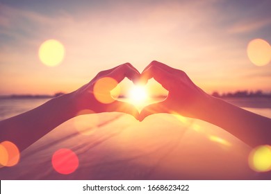 Female Hands Heart Shape On Nature Bokeh Sun Light Flare Wave And Blur Tropical Sunset Beach Abstract Background. Copy Space Of Happy Love Travel And Freedom In Nature Concept. Vintage Tone Color.