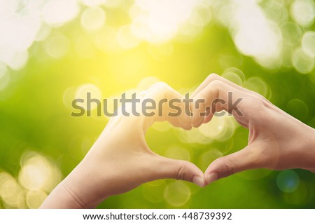 Female hands heart shape on nature green bokeh sun light flare and blur leaf abstract background. Happy love and freedom concept. Vintage tone color style.