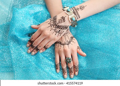 Female hands with henna tattoo on blue fabric background