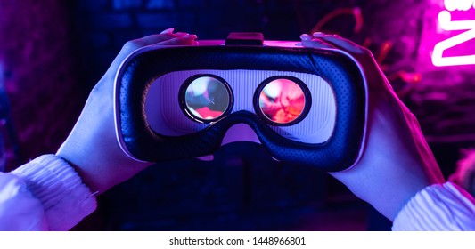 Female hands hold 3d 360 vr headset wear ar innovative glasses goggles on camera in futuristic purple neon light, girl gamer virtual augmented reality technology background concept, close up view