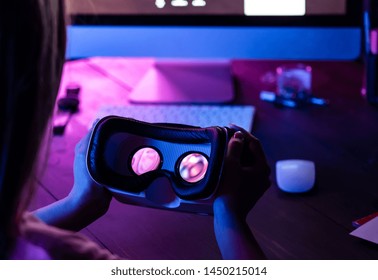 Female hands hold 3d 360 vr headset glasses goggles at work table computer background in futuristic purple neon light, girl gamer virtual augmented ar reality innovative tech concept, close up view - Powered by Shutterstock