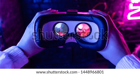 Female hands hold 3d 360 vr headset wear ar innovative glasses goggles on camera in futuristic purple neon light, girl gamer virtual augmented reality technology background concept, close up view 商業照片 © 